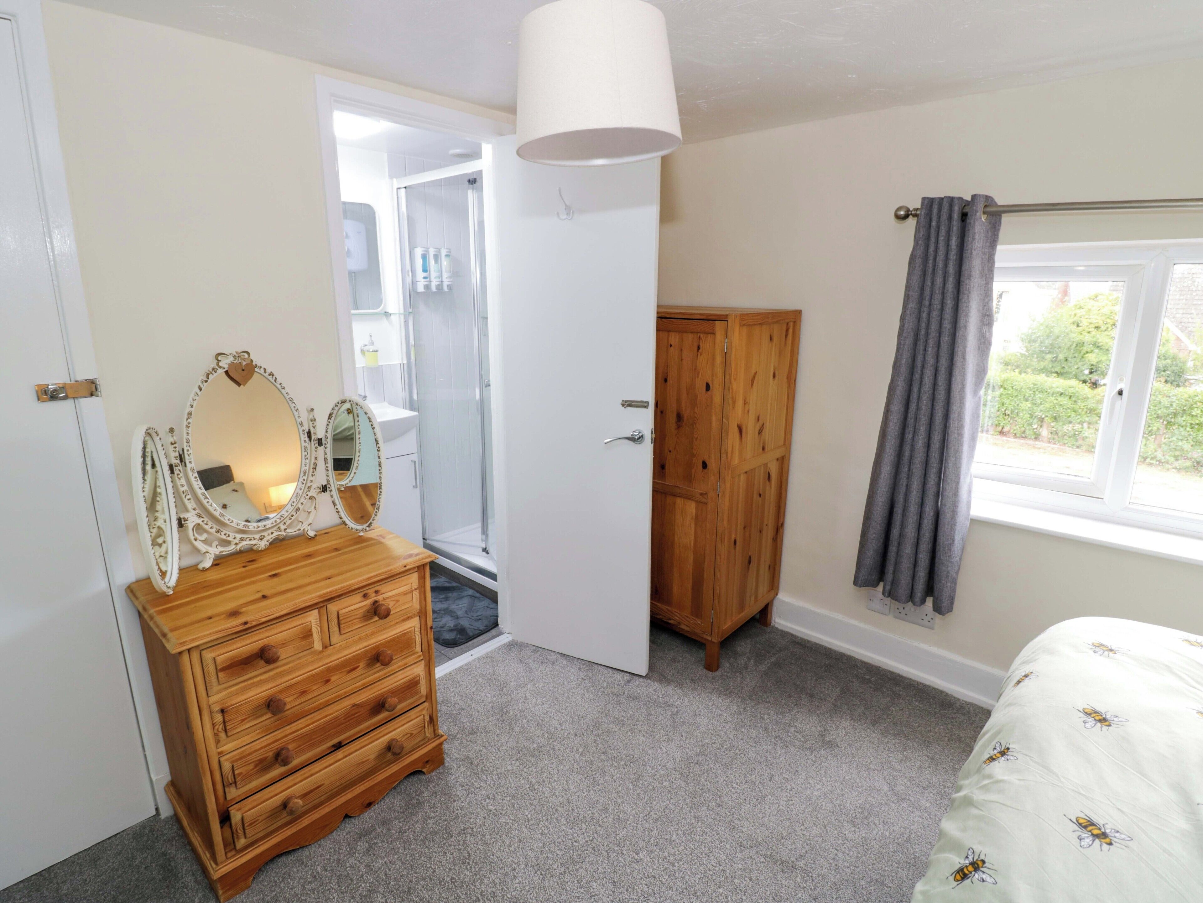 A bedroom with a wooden dresser, a mirror, a wardrobe, and a window with a curtain.