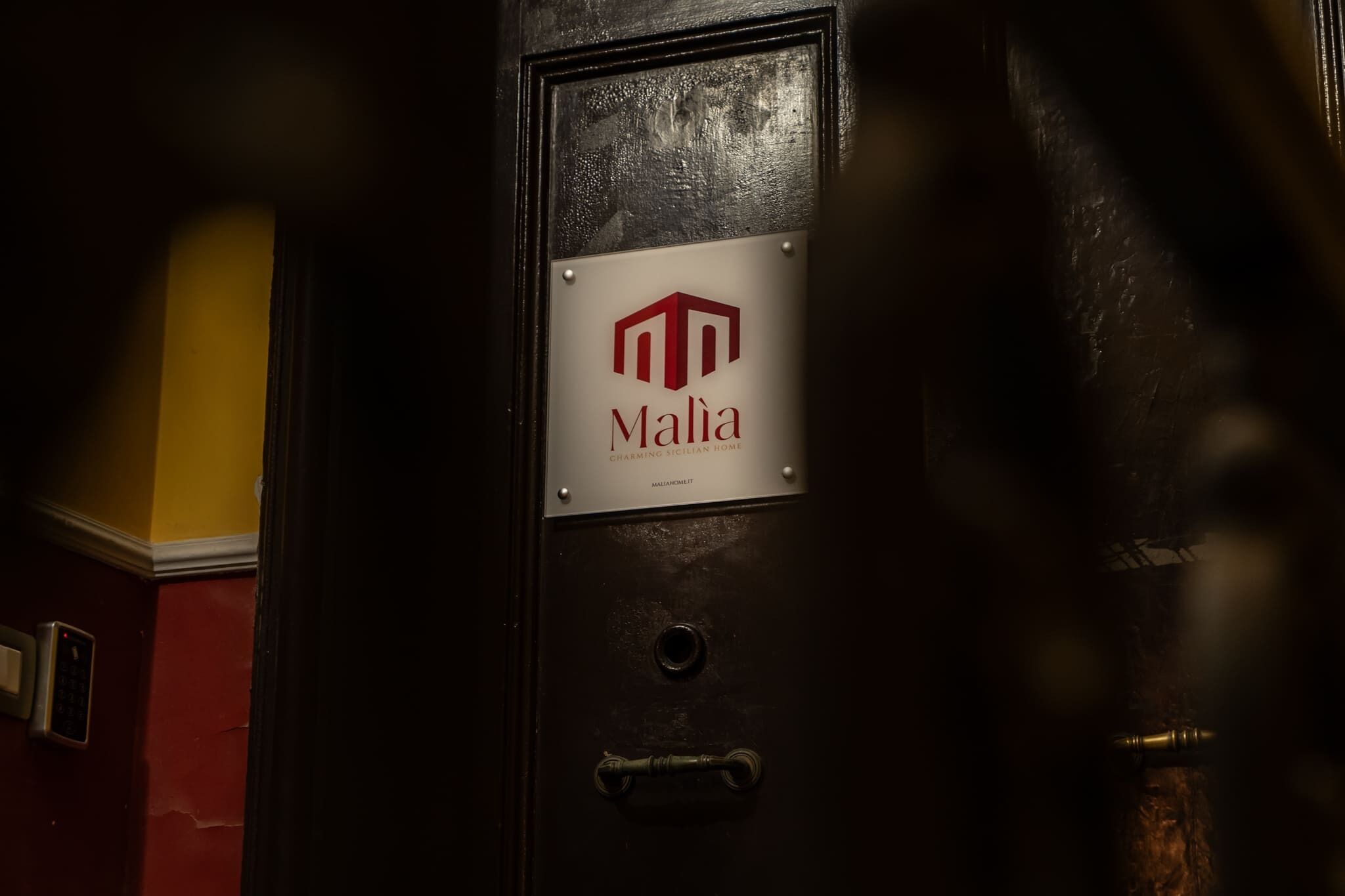 Una porta de fusta fosca amb un cartell que diu 'Malia Charming Sicilian Wine'.