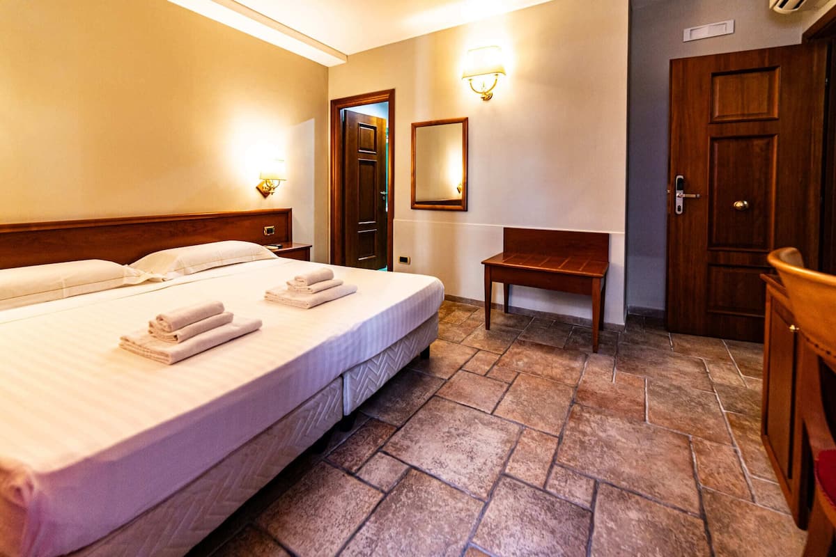 A hotel room with a large bed, a wooden bench, a mirror, and a wooden wardrobe.