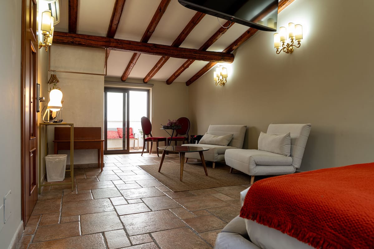 A room with a tiled floor, a sofa, a chair, a small table, and a lamp. There is a door leading to an outdoor area.
