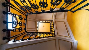 A staircase with ornate black metal railings and a yellow wall. - MALIA HOME (Catania)