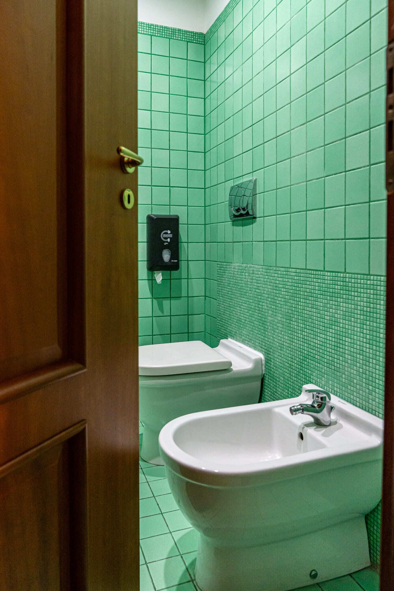 A bathroom with green tiled walls, a white sink, and a bidet.