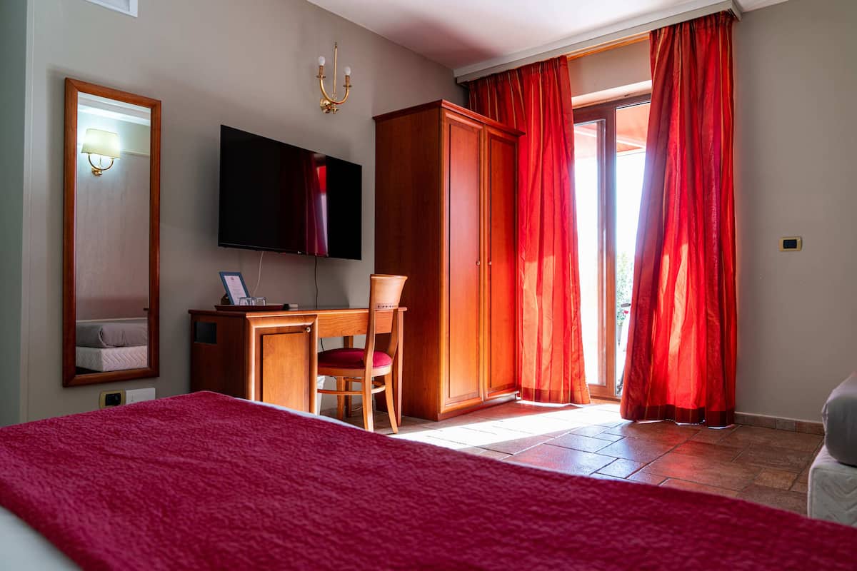 A hotel room with a bed, a desk with a chair, a television, and a wardrobe.