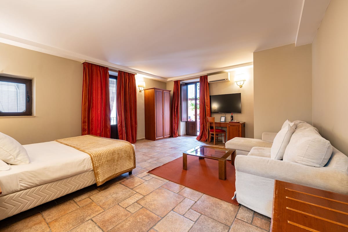 A hotel room with a bed, a sofa, a TV, and a desk with a chair.