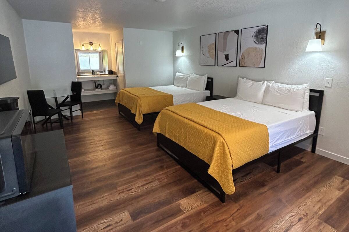 A hotel room with two beds, wooden flooring, a desk, and a mirror.