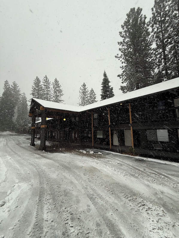 A snow-covered building with a sloped roof, a covered outdoor area, and a dirt road leading to it.