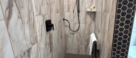 Eine Dusche mit hexagonal gefliestem Boden und Marmorwänden.