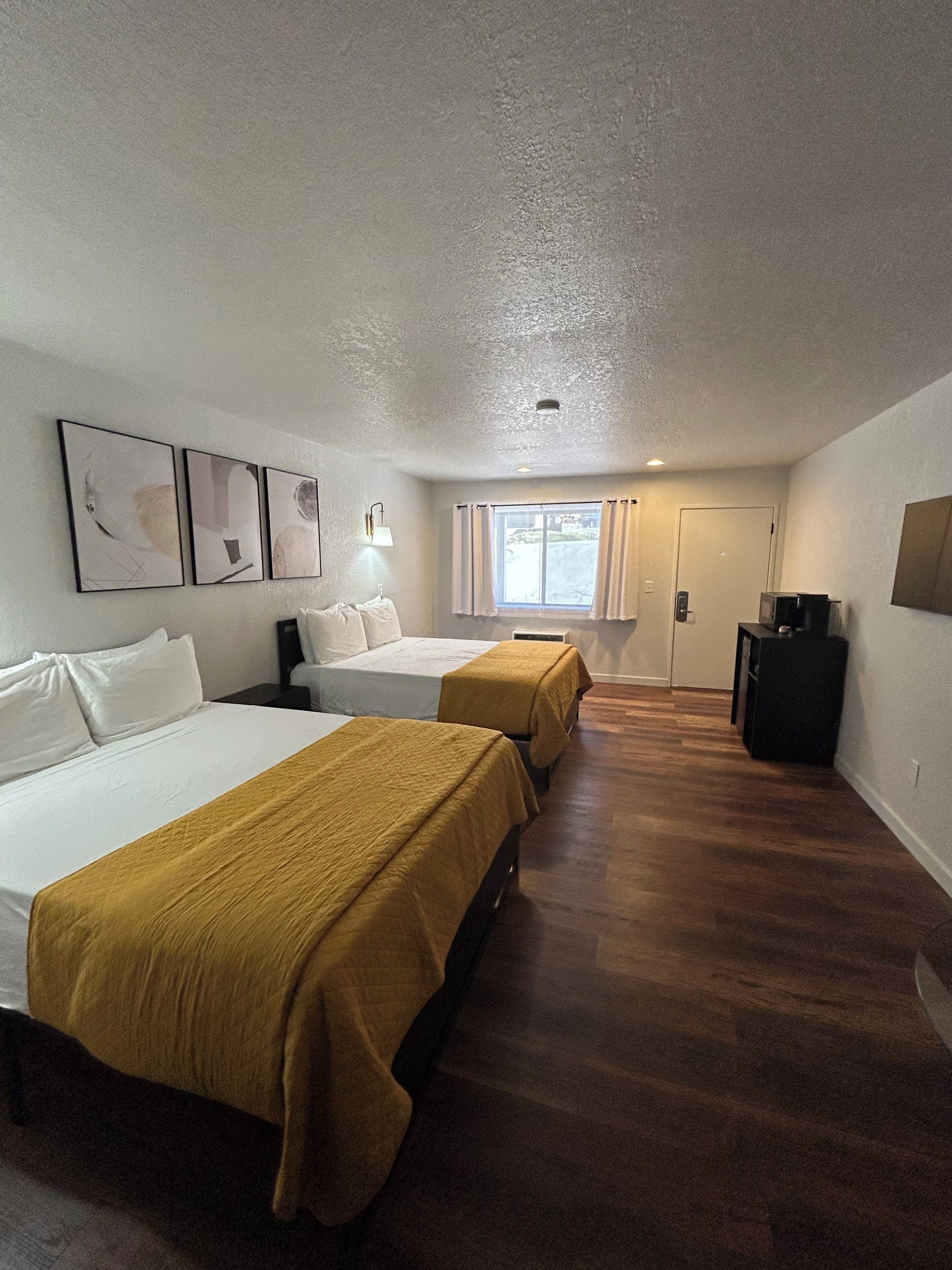 Habitación de hotel con dos camas, una ventana con cortinas, televisor montado en la pared y una obra de arte en la pared.