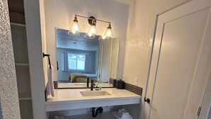 Un baño con tocador blanco, un espejo grande y una puerta.