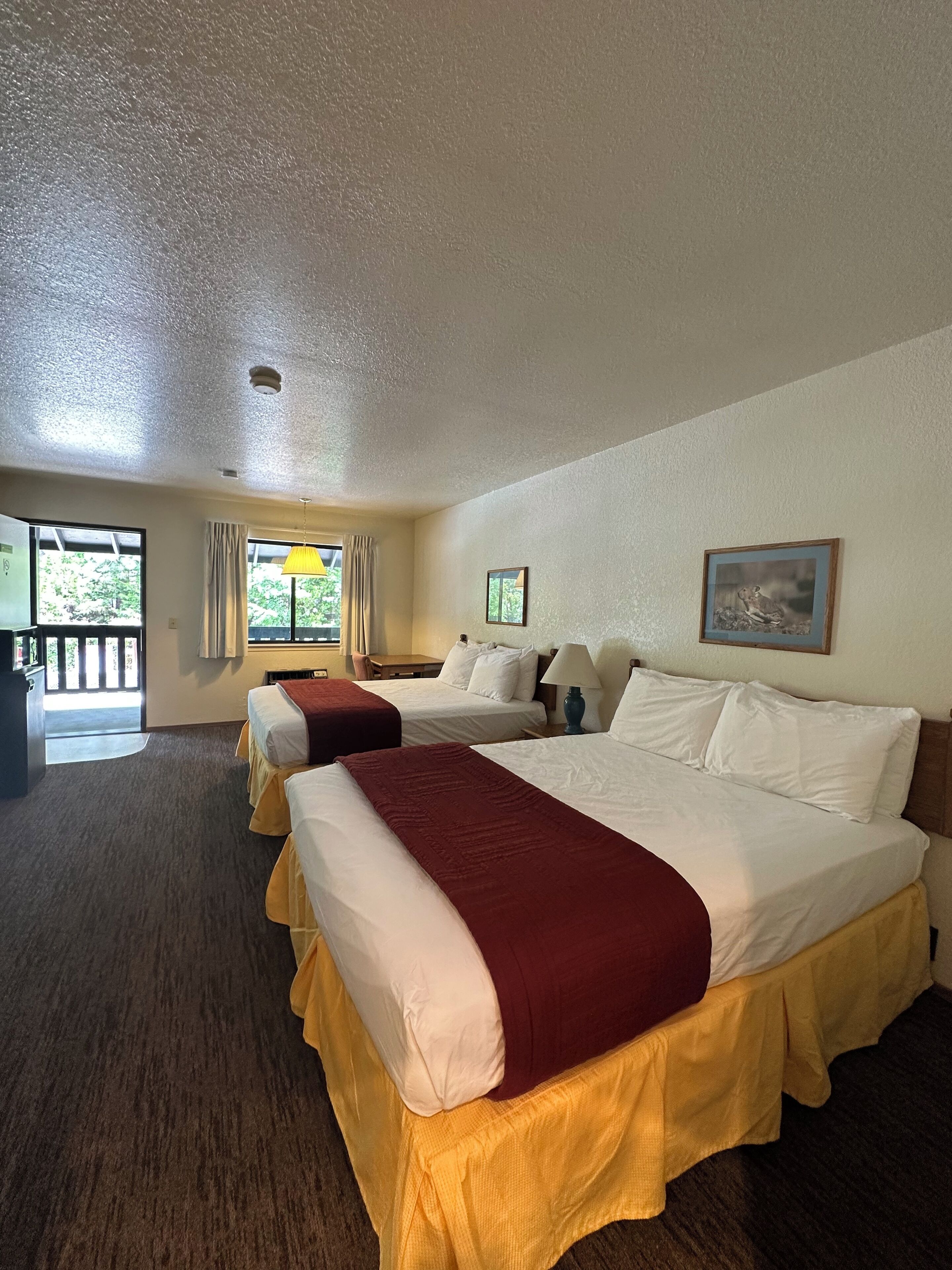 Habitación de hotel con dos camas, un escritorio y una ventana con cortinas.