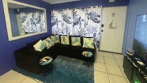 Una sala de estar con un sofá negro, un tapete azul y un televisor sobre un mueble.