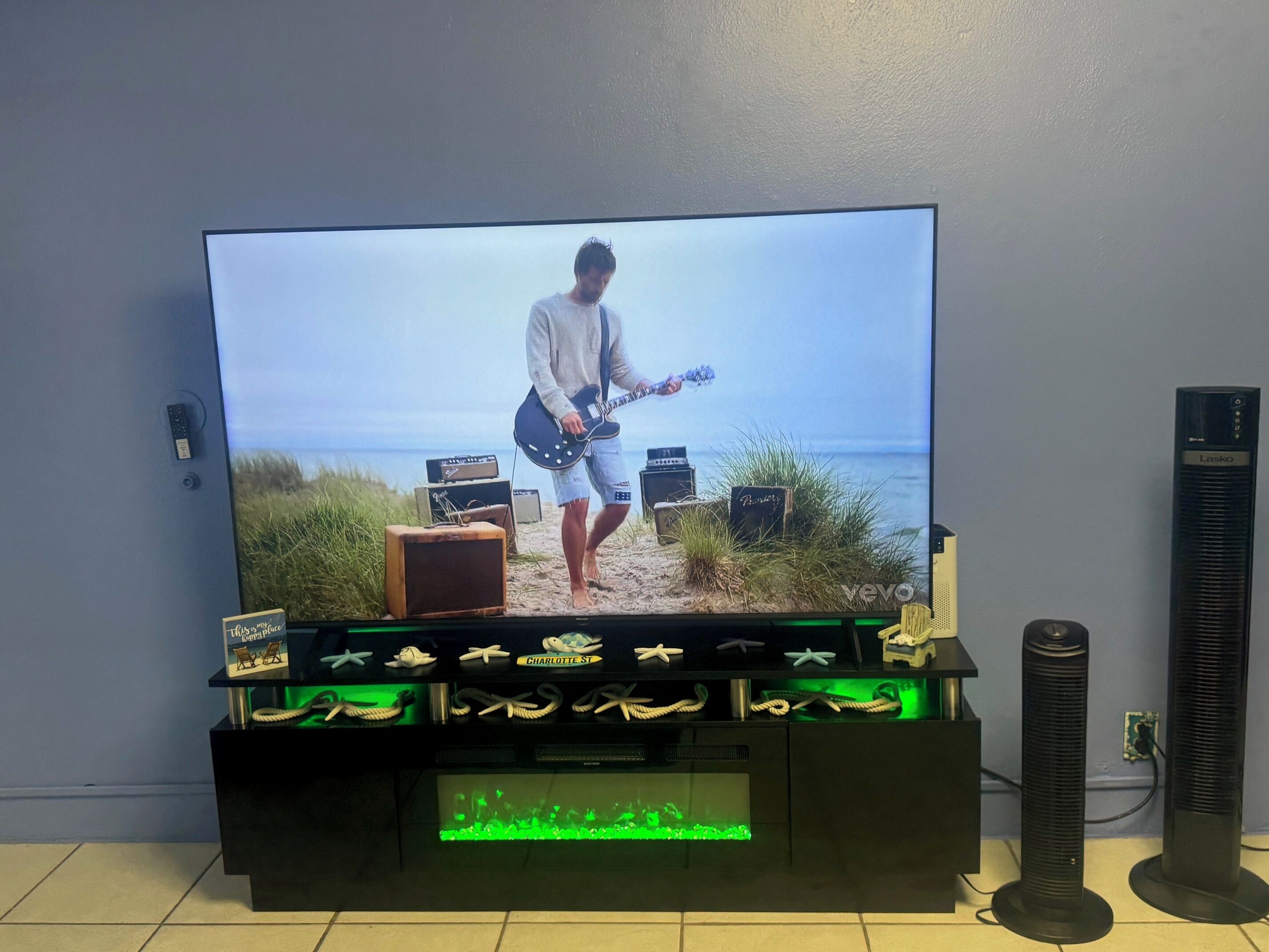 A television on a stand with a beach scene, a speaker, and a decorative shelf with items.