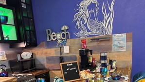 Interior de un restaurante con una mesa de madera preparada para dos comensales, una máquina de café y un cartel que dice 'Blessed Welcome'.
