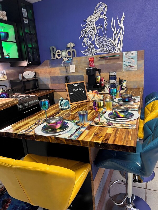 A restaurant interior with a wooden table set for dining, a coffee machine, and a sign that reads 'HELLO & WELCOME'.