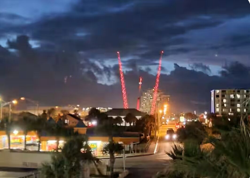 A nighttime cityscape with illuminated buildings and a prominent red-lit tower structure.