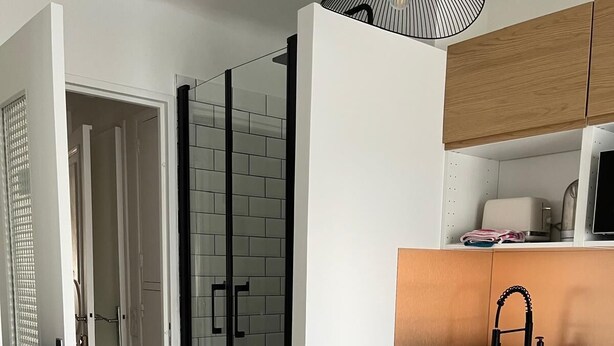 Une cuisine moderne avec des meubles en bois, un four à micro-ondes encastré et une cabine de douche en verre.