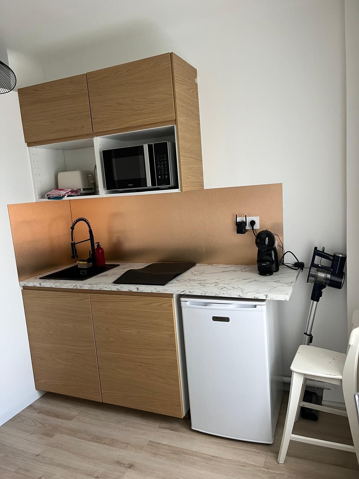 A compact kitchen with wooden cabinets, a microwave, a sink, a coffee maker, and a small refrigerator.