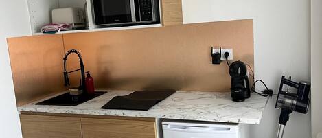 A compact kitchen with wooden cabinets, a microwave, a sink, a coffee maker, and a small refrigerator.