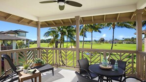 Uma área externa coberta com mesa e cadeiras, um ventilador de teto e vista para um campo de golfe.