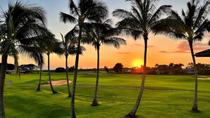 Um campo de golfe com palmeiras e um pôr do sol ao fundo.