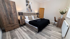 A modern bedroom with a large bed, wooden wardrobe, bedside lamps, and a decorative wall piece. - Tŷ Haul (Sun House) is not your typical holiday let. (Cefn-mawr)