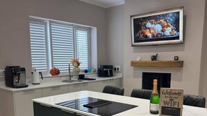 A modern kitchen with a central island, a coffee machine, a bottle of champagne, and a sign indicating WiFi availability. - Tŷ Haul (Sun House) is not your typical holiday let. (Cefn-mawr)