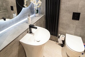 A modern bathroom with a white sink, black faucet, and a toilet. There is a mirror above the sink and a small potted plant on the counter.