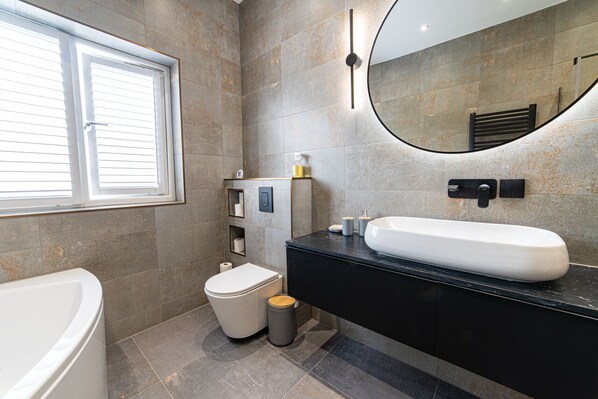 A modern bathroom with a white bathtub, a black vanity with a large sink, and a toilet.
