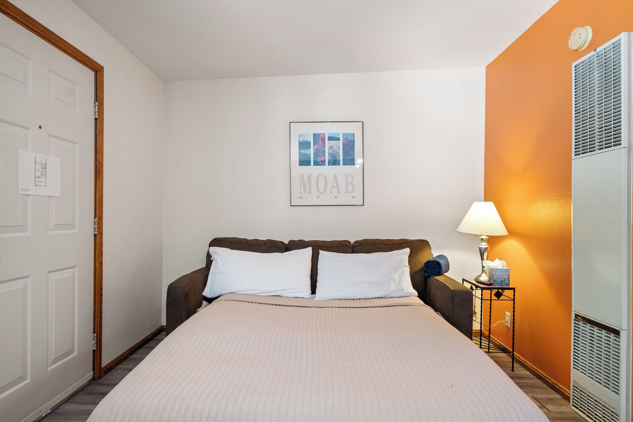 A hotel room with a bed, a nightstand, a lamp, and a framed picture on the wall.