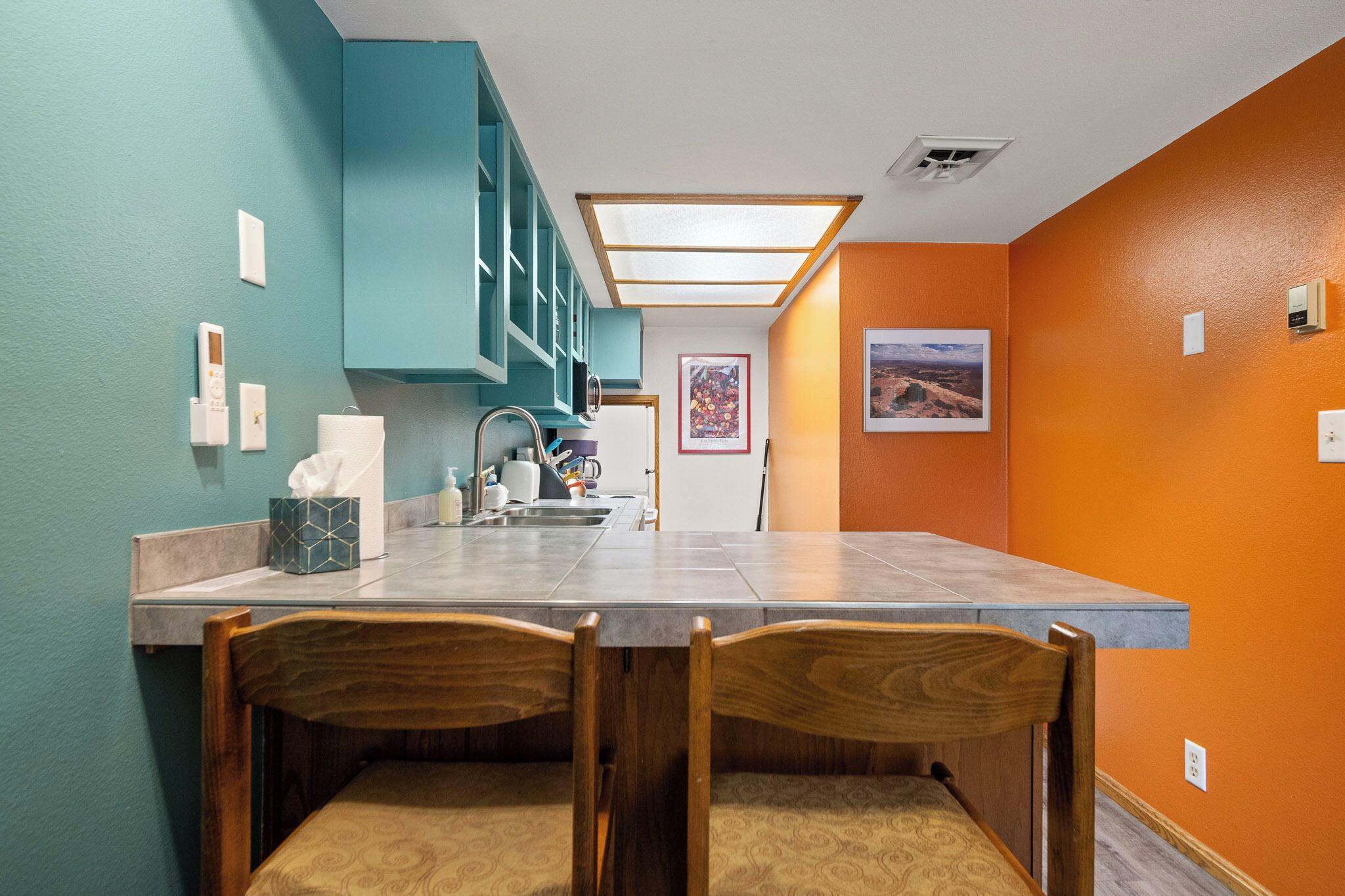 Une cuisine avec des armoires de couleur turquoise, un comptoir et un évier. On y trouve deux chaises en bois et une petite table.