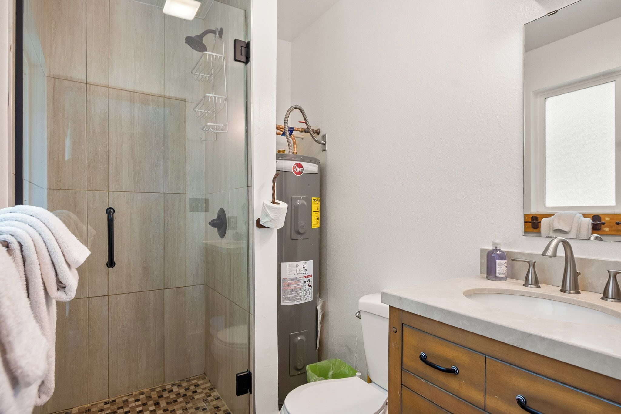 Un baño moderno con cabina de ducha de vidrio, inodoro, lavabo con espejo y barra para toallas.