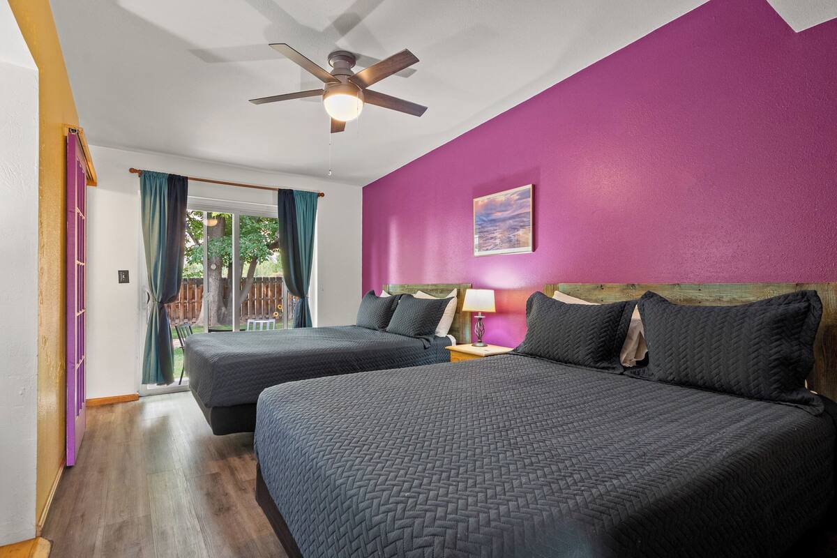 A room with two beds, a ceiling fan, a window with curtains, and a purple wall.