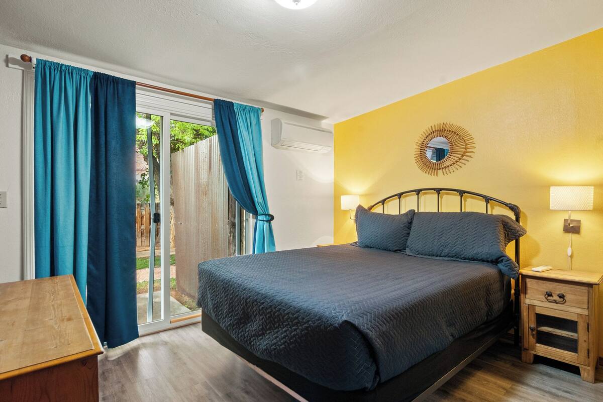 A bedroom with a bed, a nightstand, a lamp, and a view of the outdoors through a sliding door.