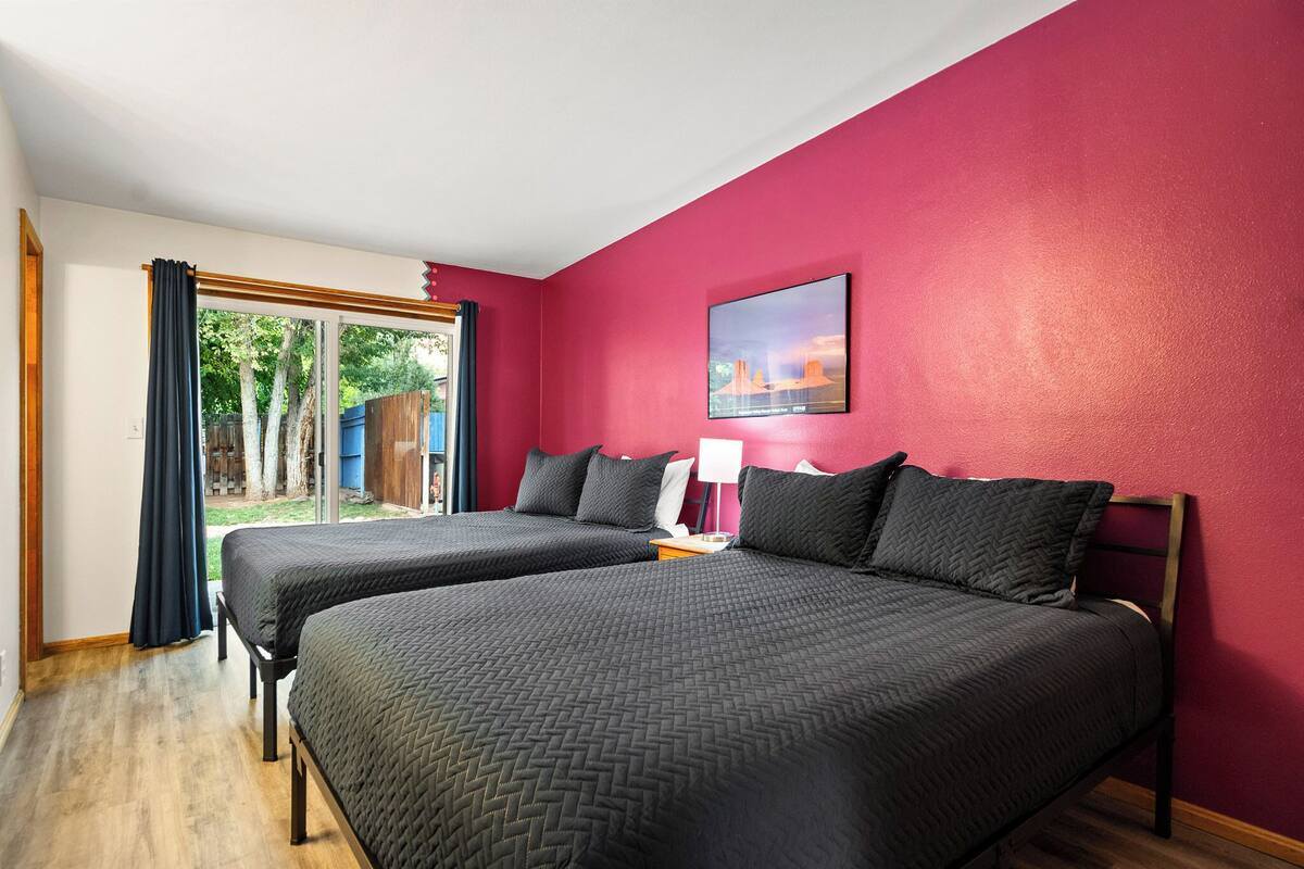 A hotel room with two beds, a red wall, a window with curtains, and a painting.