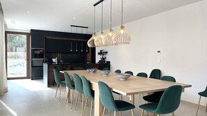 Een moderne keuken met een grote eettafel en stoelen, een inbouwoven en hanglampen.