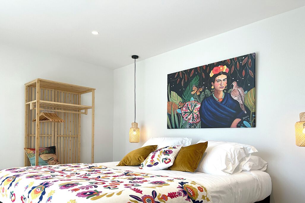 Une chambre à coucher comprenant un lit, une armoire en bois, un tableau accroché au mur et deux appliques murales.