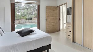 Een slaapkamer met een bed, een televisie, een houten garderobe en een glazen schuifdeur naar een zwembad.