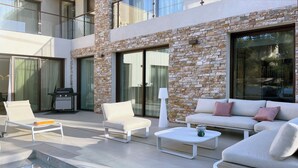 Een moderne buitenruimte met een zwembad, lounge fauteuils, een bank en een barbecue.