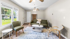 A living room with a sofa, chairs, a coffee table, a ceiling fan, and a view of the outdoors through large windows.
