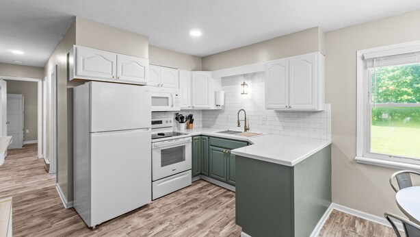 A modern kitchen with white cabinets, a green island, and a view of the outdoors.