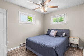 A bedroom with a bed, a nightstand, a ceiling fan, and two windows. - Quaint Rennovated 2-Bedroom close to the solar farms and Honda (Raymond)