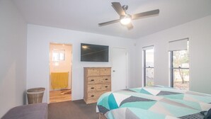 A bedroom with a bed, a wooden dresser, a television on the wall, and a ceiling fan. - Azure on Bondi Place (Kingscliff)