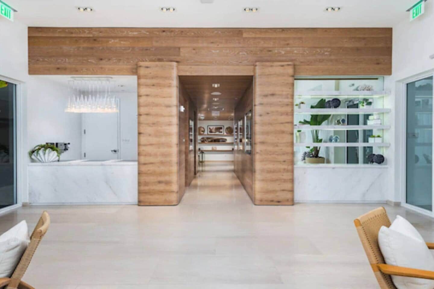 Een moderne hotel lobby met een centrale houten kolom, een receptiebalie en een plantenpresentatie.