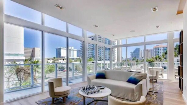 A spacious living area with large windows, a sofa, two armchairs, and a coffee table. - Fort Lauderdale Luxe - Beach + Rooftop Pools (Fort Lauderdale)