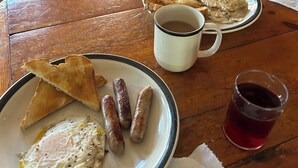 Una mesa de madera con alimentos para el desayuno, incluyendo tostadas, salchichas y un huevo frito.