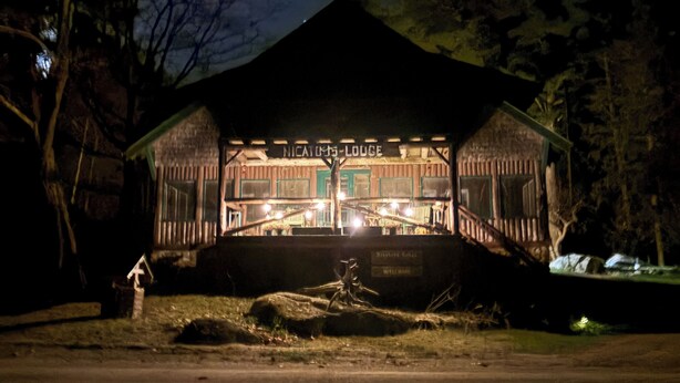 Un refugio rústico con un porche cubierto y un letrero que dice "Nicaio's Lodge".