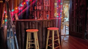 Un área de bar con paredes de madera, una barra y dos taburetes. Hay esquíes apoyados en la pared y un soporte para esquíes.