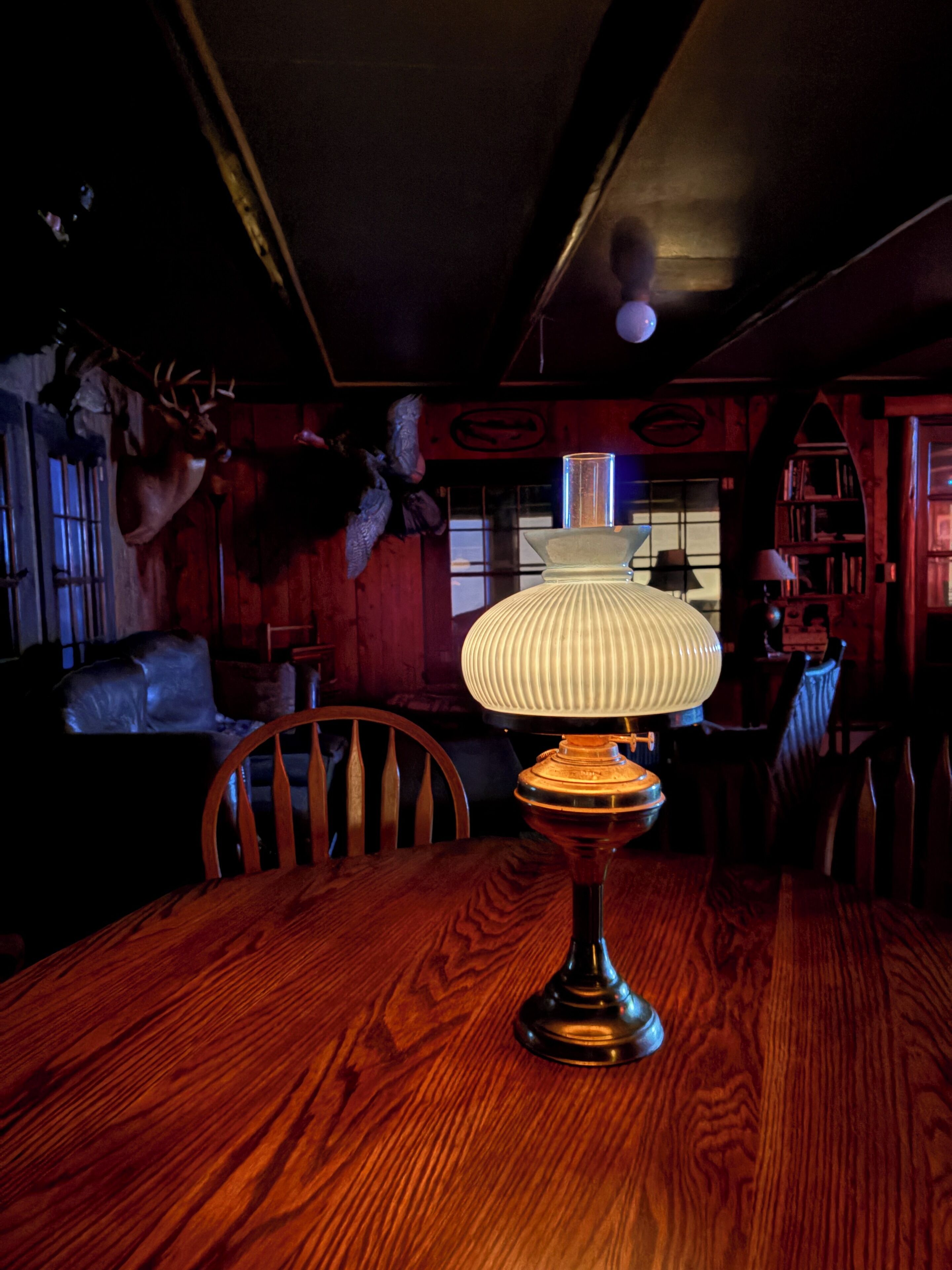A wooden table with a lamp in a dimly lit room with wooden walls and a ceiling with exposed beams.