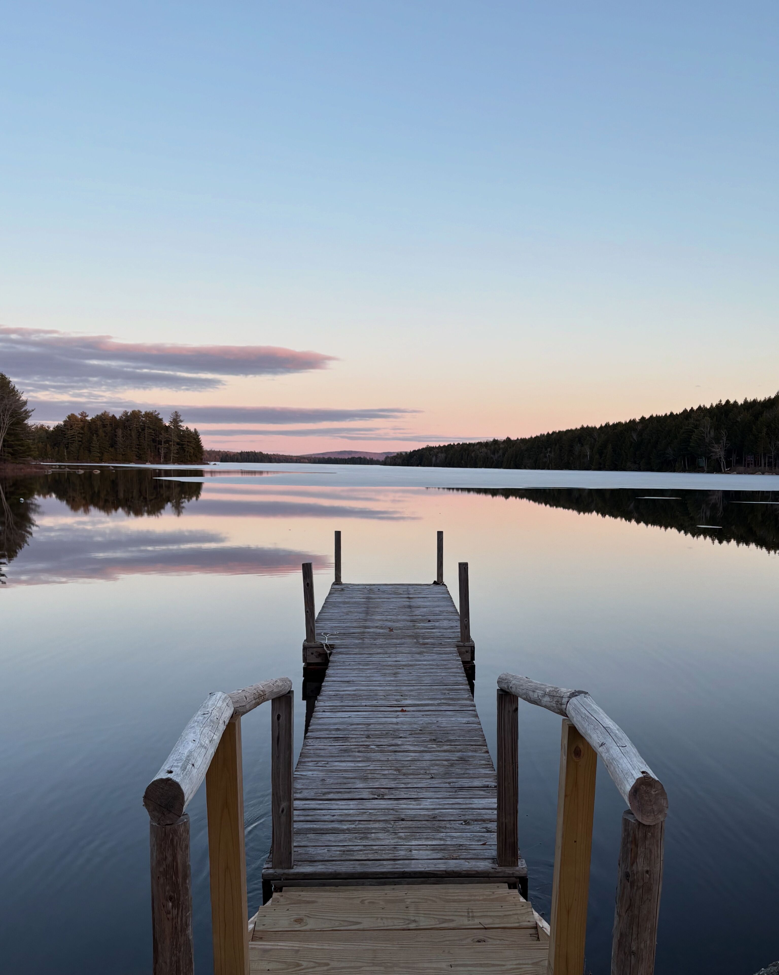 A wooden pier extending into calm water with a forested shoreline in the background.