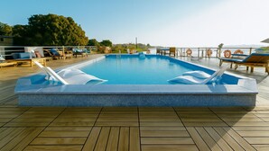 Ein rechteckiger Pool mit Holzterrasse, Liegestühlen und einer Brüstung.